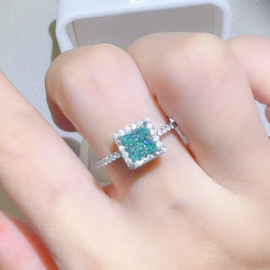Radiant square halo moissanite ring in silver with a bright teal center stone.