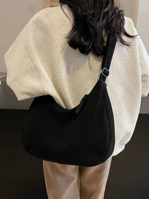 Black corduroy crescent shoulder bag with braided detail and adjustable strap.