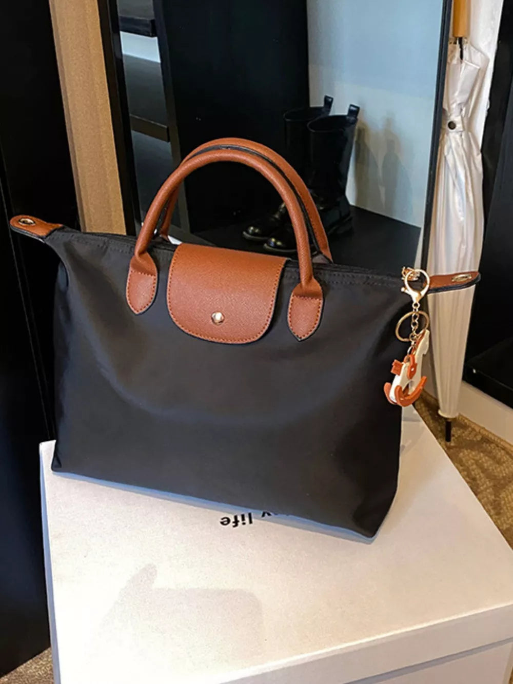 Black nylon tote bag with brown leather accents and a keychain charm