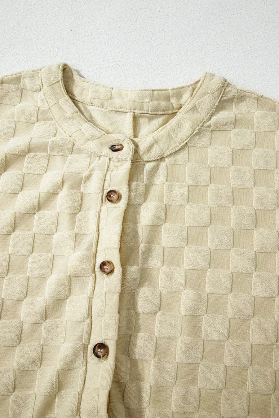 Textured sleeveless wide-leg romper in cream with a checkered pattern and band collar.