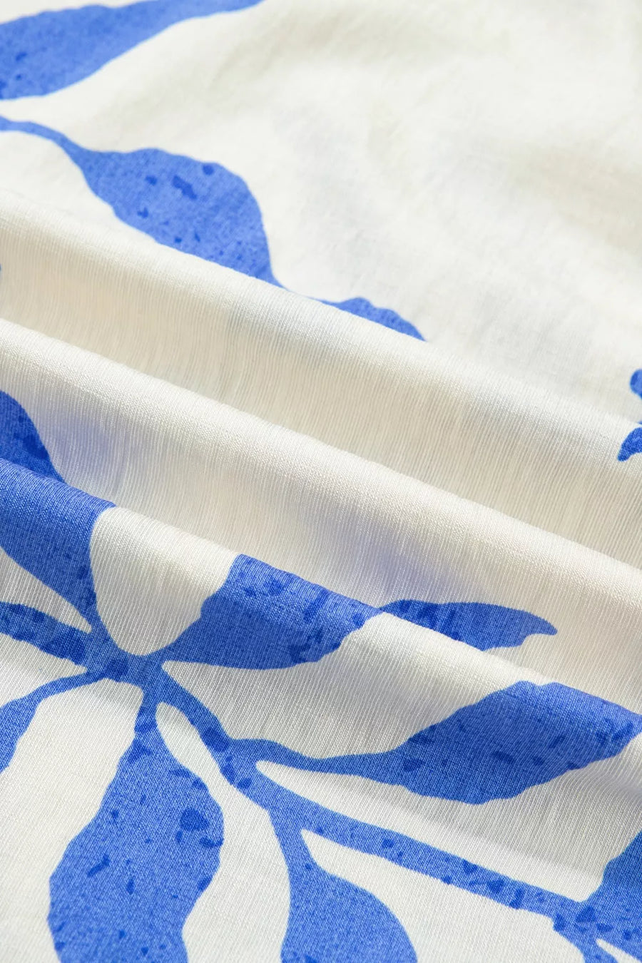 Maxi dress with blue botanical print on white fabric, showing texture and folds.