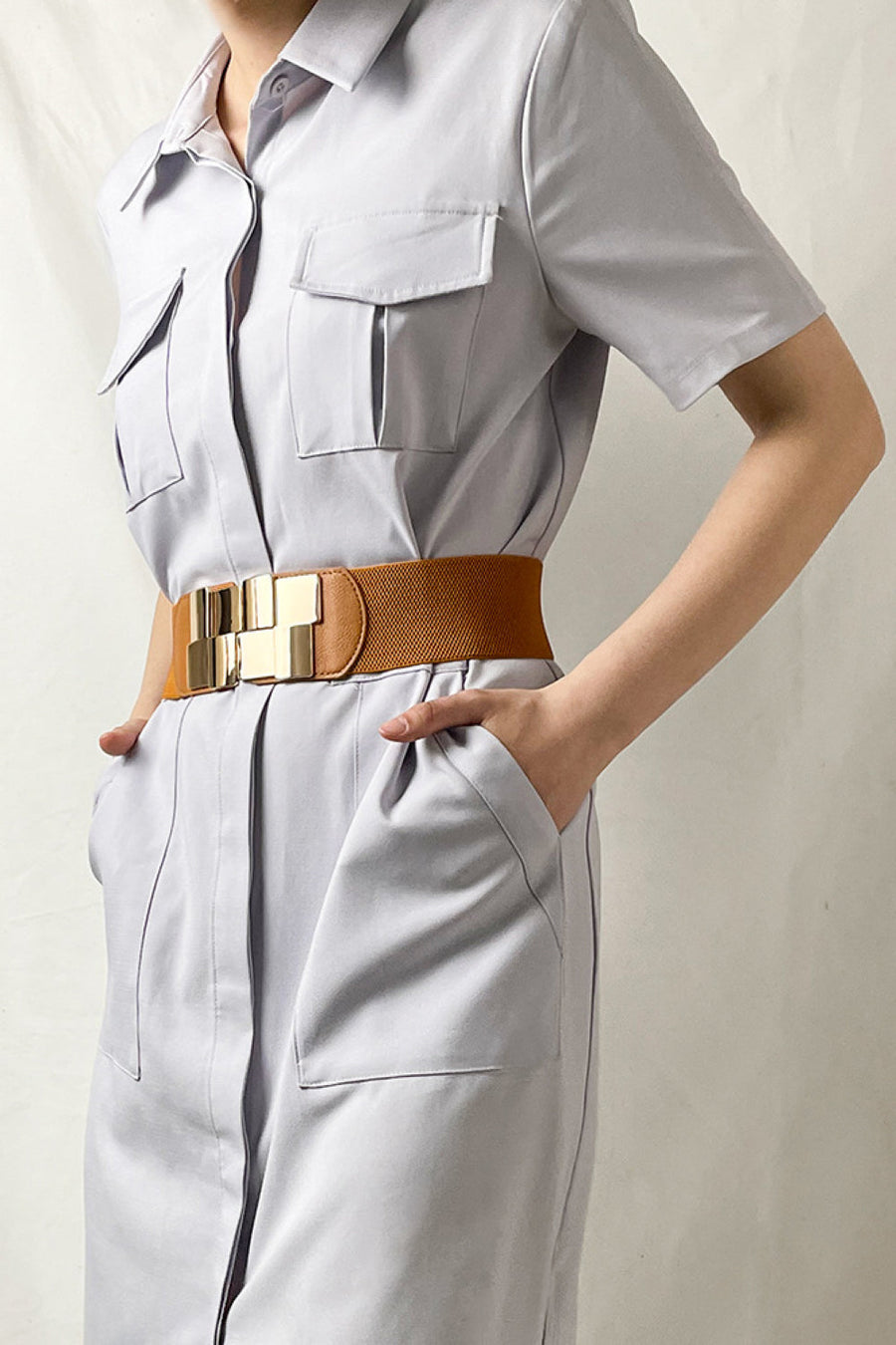 Caramel elastic belt with geometric gold buckle, cinching a light gray dress.