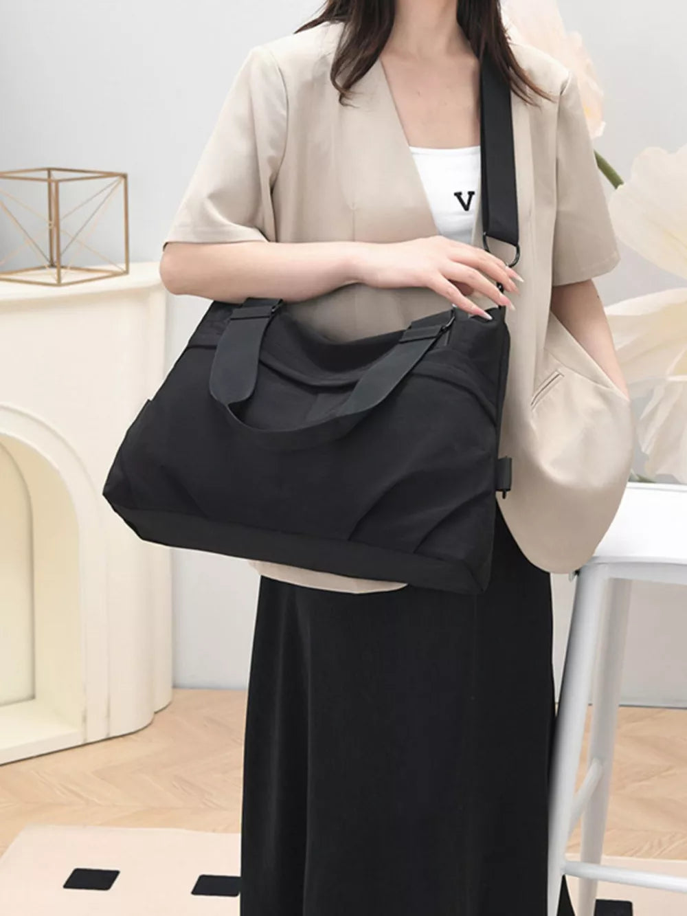 Black canvas tote bag with double straps and a crossbody strap, worn by a woman in a beige blazer.