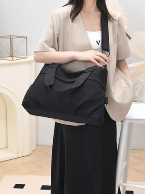 Black canvas tote bag with double straps and a crossbody strap, worn by a woman in a beige blazer.