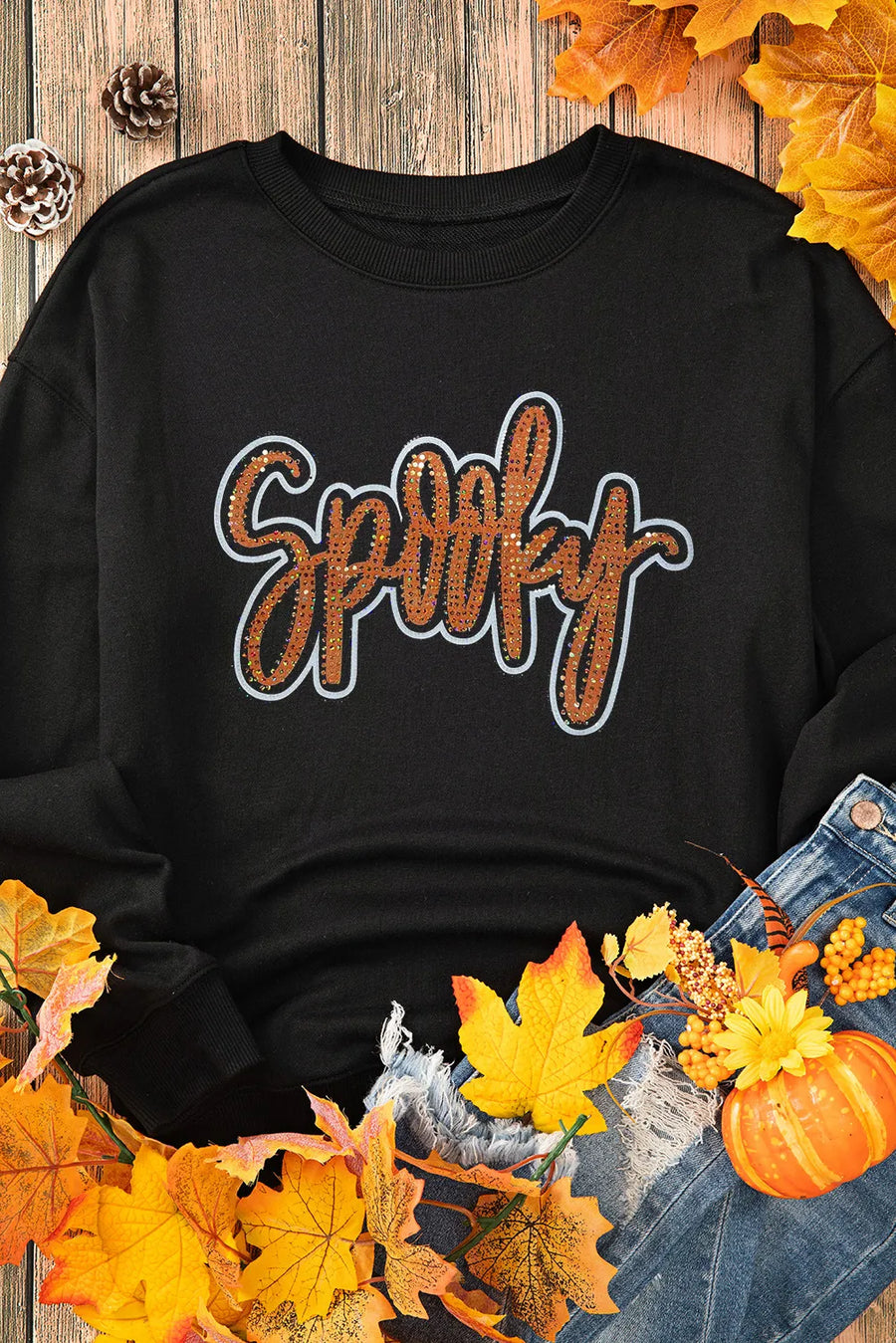 Black crewneck sweatshirt with "Spooky" script graphic embellished with orange sequins.