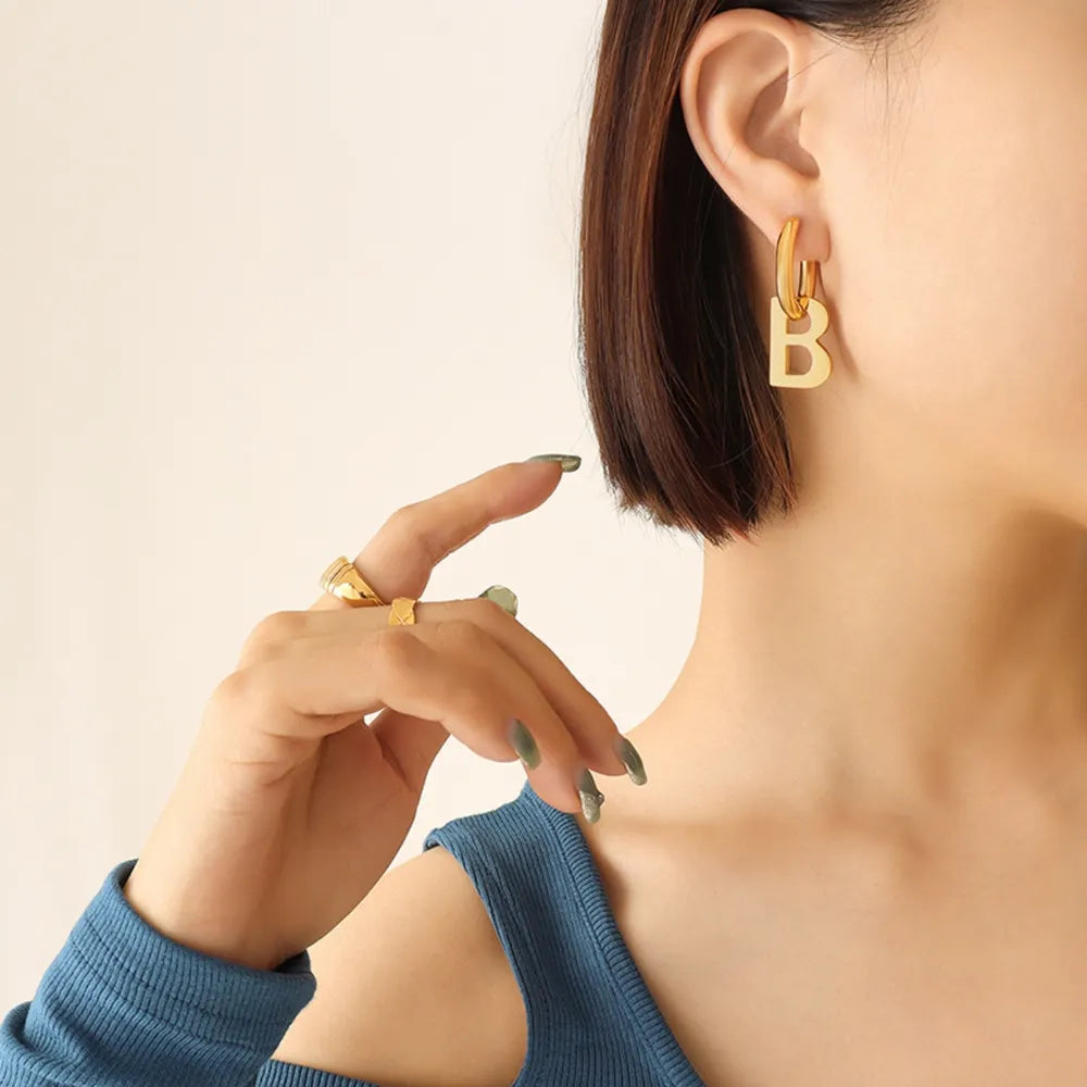Gold letter B statement hoop earrings made of titanium, styled with rings.