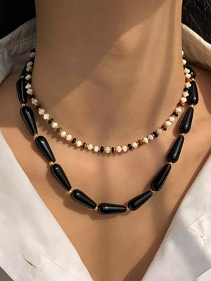 Black teardrop agate choker necklace with gold accents and a delicate beaded necklace layered above.