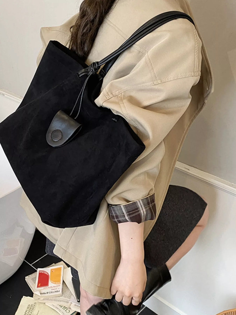 Large black suede tote bag with leather strap and button detail.