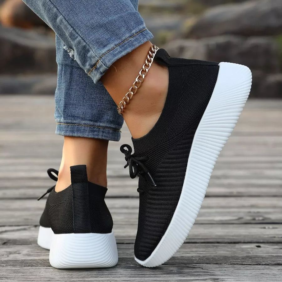 Black lace-up sneakers with white mid sole and ribbed texture.