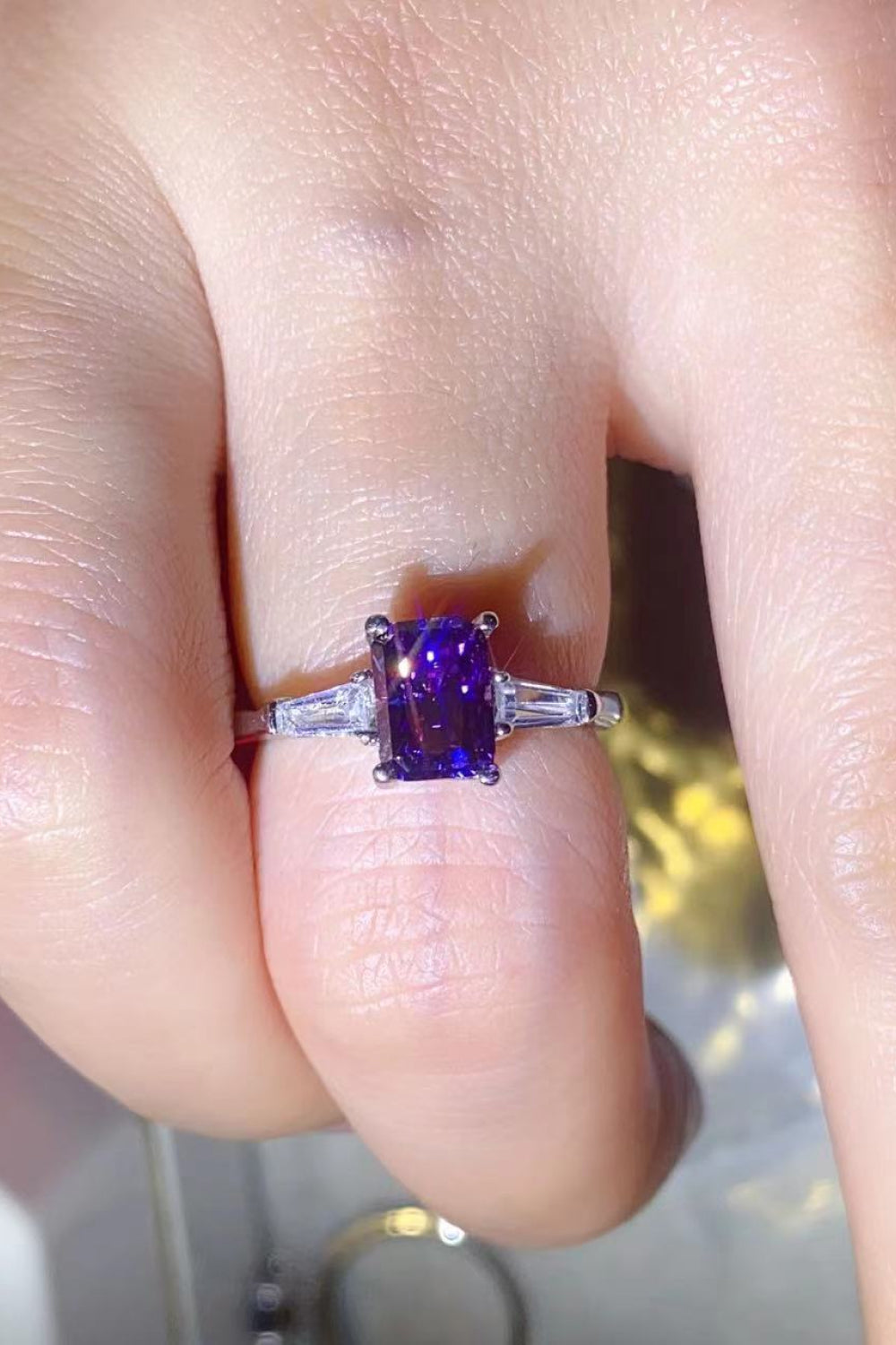 Purple emerald-cut moissanite and baguette platinum ring with accent stones.