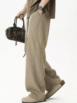 Khaki men's track pants with drawstring waist and wide leg, styled with a brown t-shirt and bag.