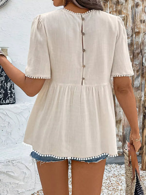 Cream babydoll blouse with pom-pom trim, puff sleeves, and button back detail.
