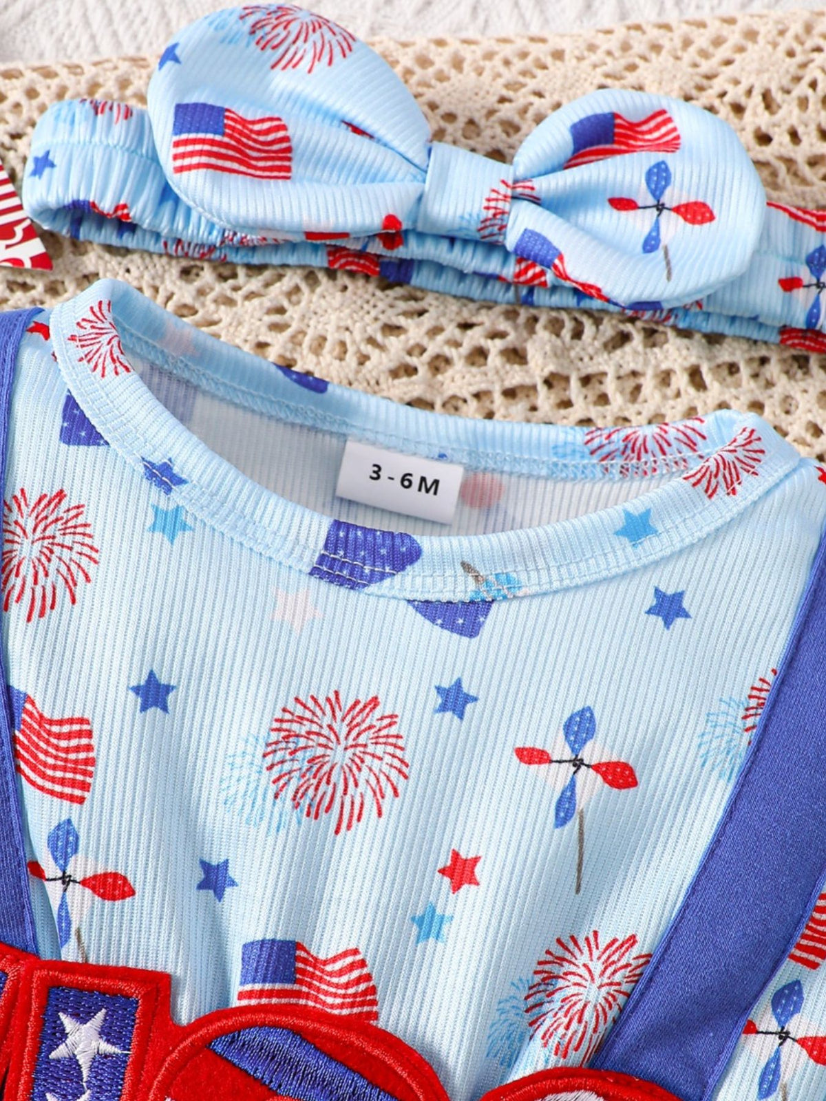 Baby blue cotton one-piece with patriotic fireworks, flags, and stars print. Includes matching headband.