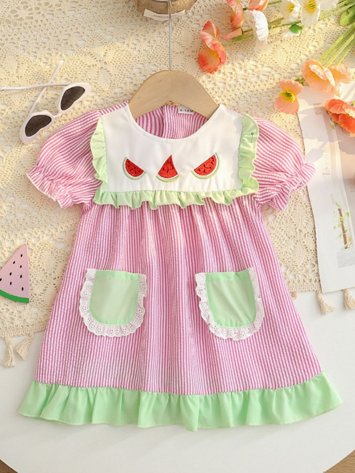 Baby dress in pink stripes with watermelon embroidery, green trim, and pockets.