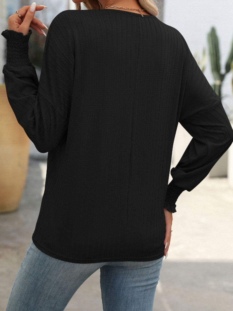 Black textured blouson top with smocked cuffs and long sleeves.
