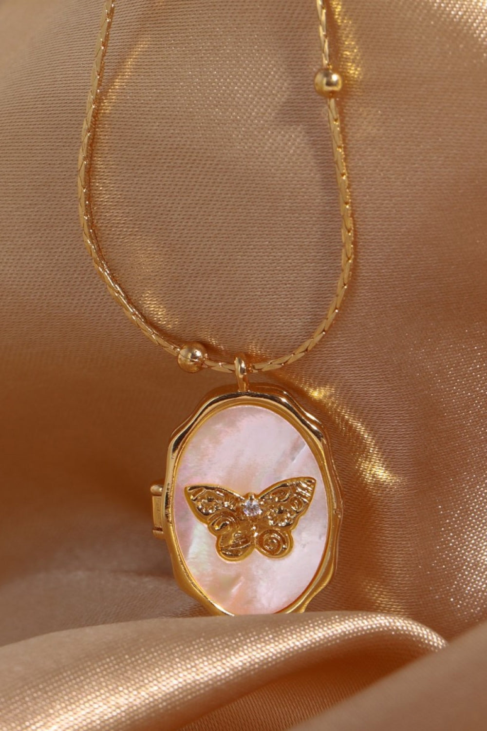 Gold locket necklace with oval mother of pearl inlay and ornate butterfly charm.