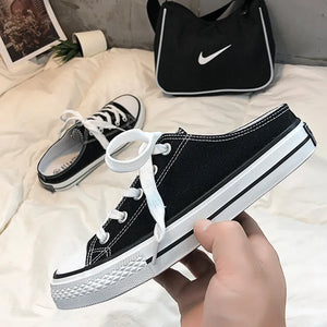 Black canvas mule sneakers with white contrast trim and laces.