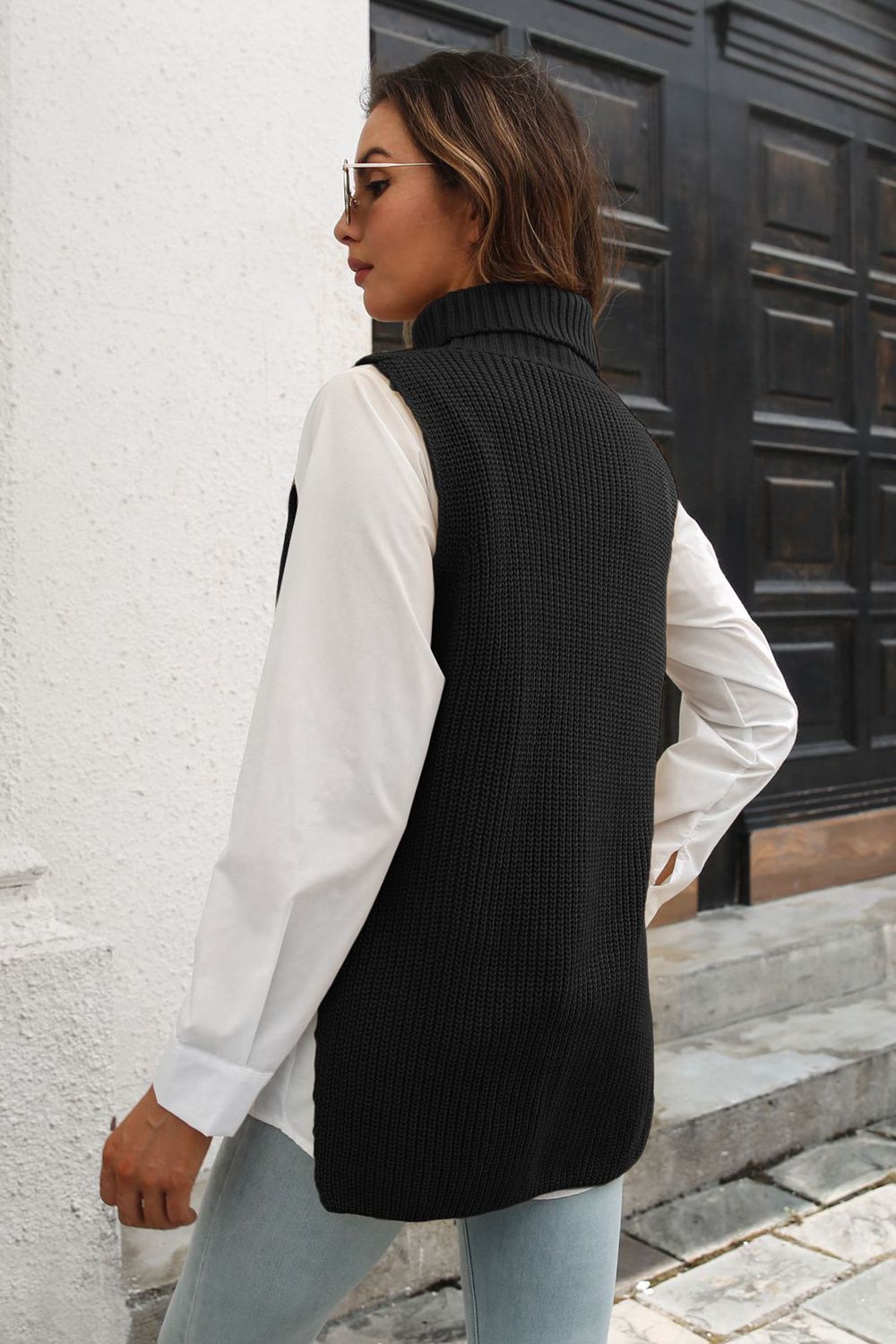 Black ribbed knit turtleneck vest with side buttons, acrylic, worn over a white shirt.