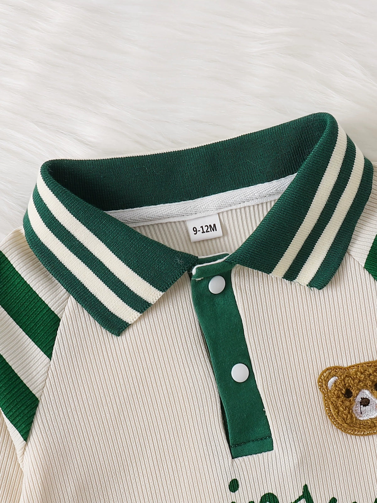 Baby one-piece with beige ribbed fabric, green striped collar, and bear applique.