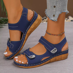 Dark blue adjustable wedge sandals with white stitching and hook-and-loop straps.