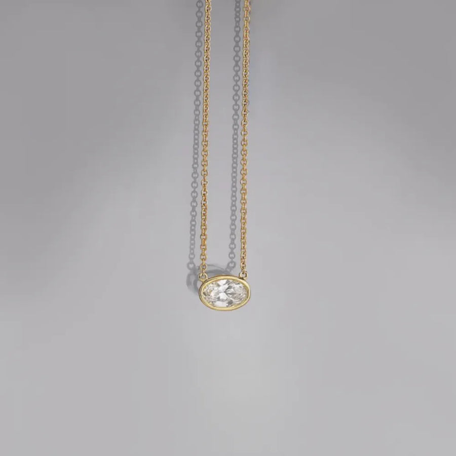 Bezel-set oval diamond solitaire necklace on a delicate 18K gold-plated chain.