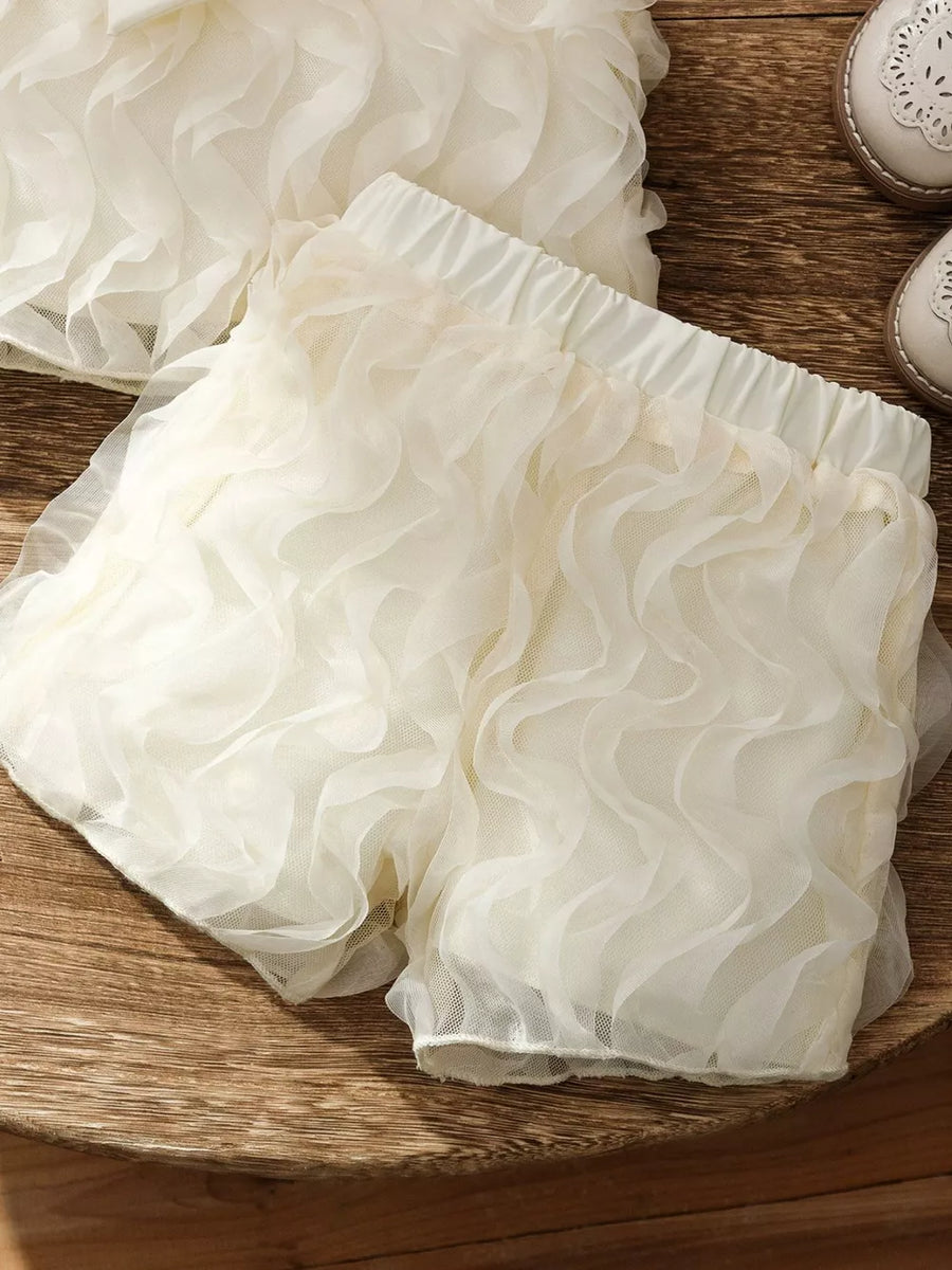 Cream ruffled baby shorts with elastic waist and sheer overlay.