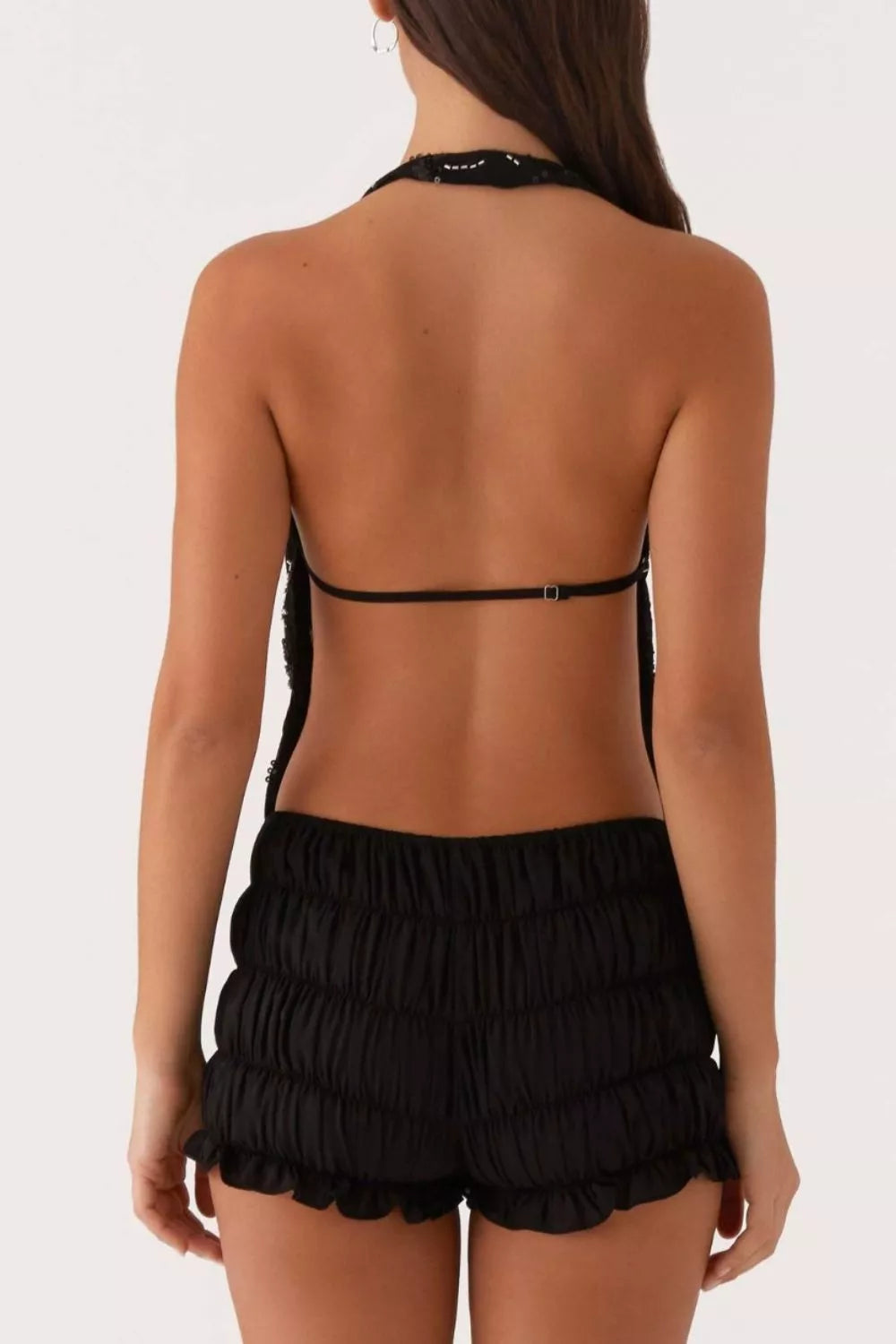 Black sequin halter crop top with adjustable strap and ruched shorts with ruffled hem.
