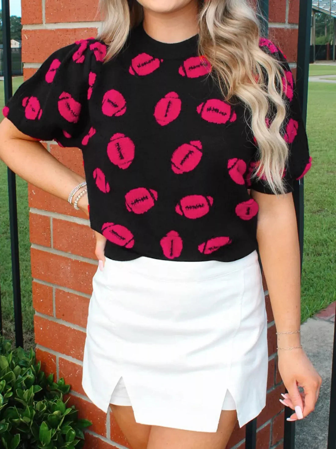 Black short-sleeve knit sweater with a pink football print and puff sleeves.