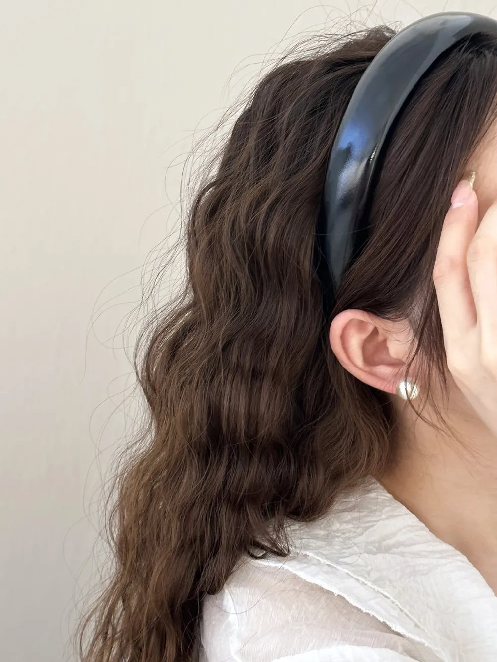 Glossy padded headband in black, styled with wavy brown hair and a white shirt.