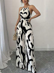 Elegant wide-leg jumpsuit with abstract black and white print, halter neck, and tie waist.