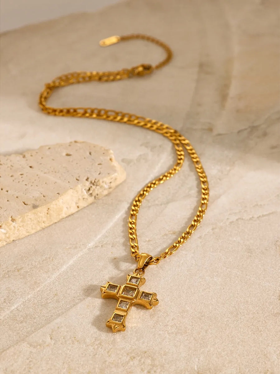 Gold cross pendant necklace with clear zirconia accents on a figaro chain.