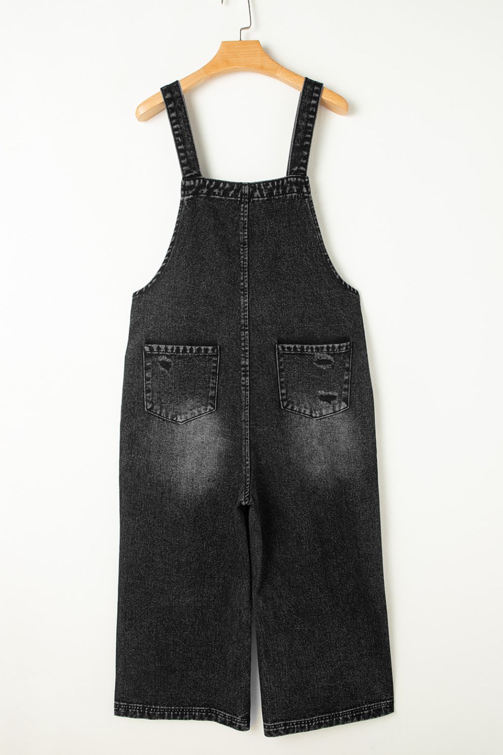 Black denim culotte overalls with distressed details and wide legs.
