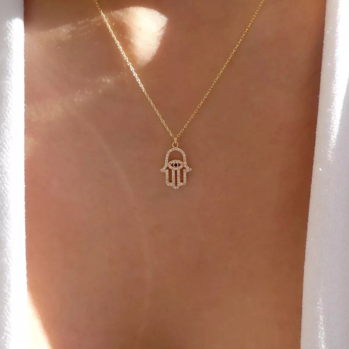 Gold evil eye hamsa pendant necklace with rhinestones on a delicate chain.