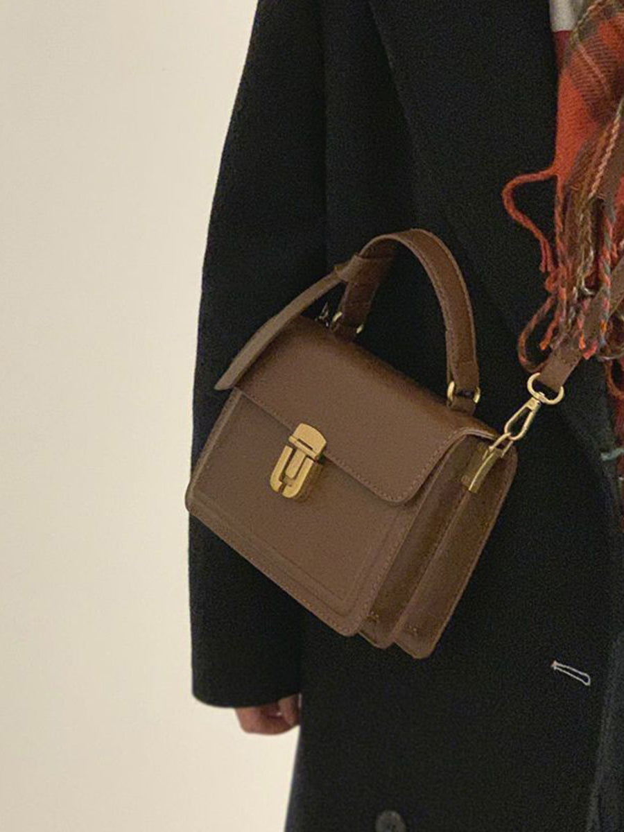 Small coffee pu leather crossbody bag with gold clasp and top handle.