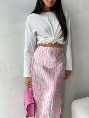 Pink and white zebra print satin midi skirt with a white knotted long sleeve top and pink handbag.