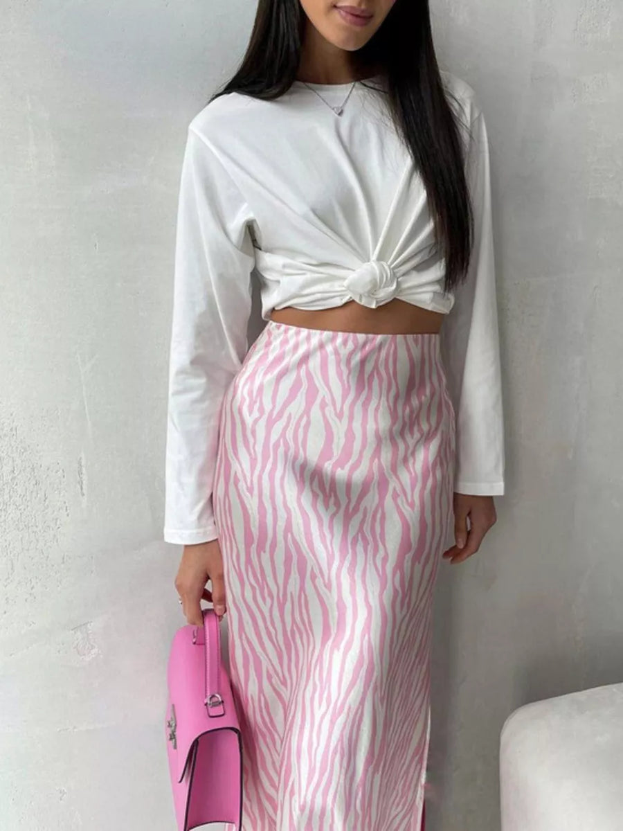 Pink and white zebra print satin midi skirt with a white knotted long sleeve top and pink handbag.