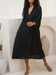 Black midi dress with tie-neck, puff sleeves, and tassel details.