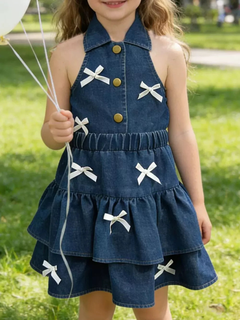 Charming denim halter dress with white bow accents and tiered skirt.