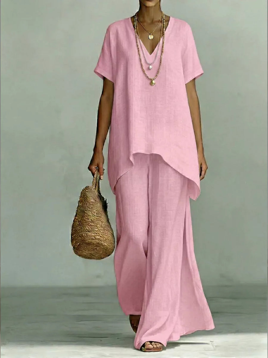 Pink linen V-neck short sleeve tunic with wide leg pants, styled with layered necklaces and a straw bag.
