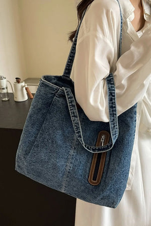 Denim shopper tote bag with leather trim detail and zipper accent.