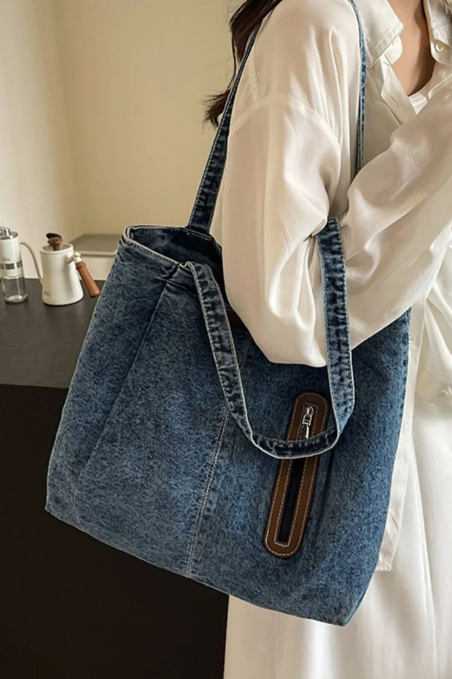 Denim shopper tote bag with leather trim detail and zipper accent.