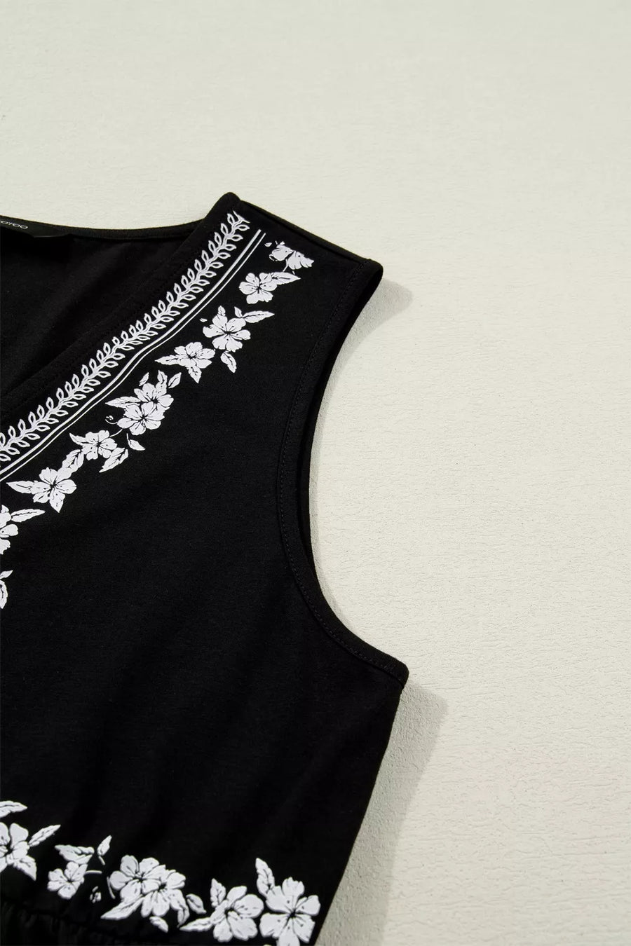 Black sleeveless v-neck top with white floral embroidery along the neckline and hem