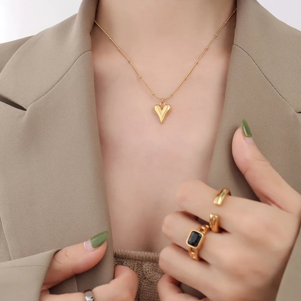 Gold heart pendant necklace with beaded chain, worn with rings.