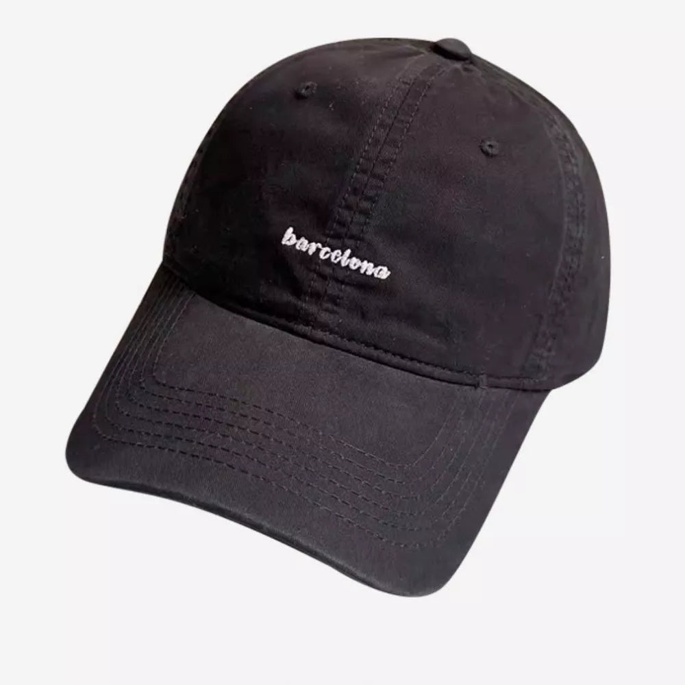 Black baseball cap with white embroidered "barcelona" text and curved brim.