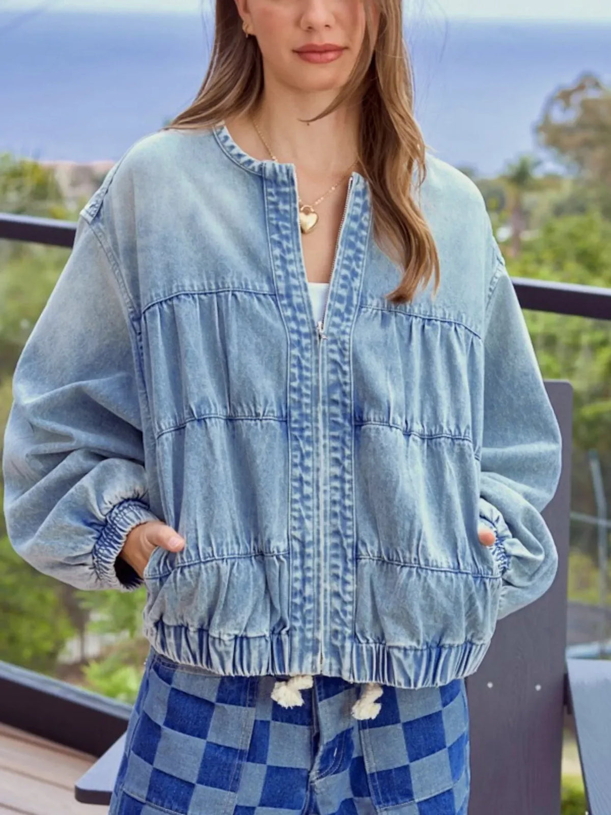 Washed denim zip-up jacket with elastic cuffs and hem, featuring a gathered yoke and sleeves.