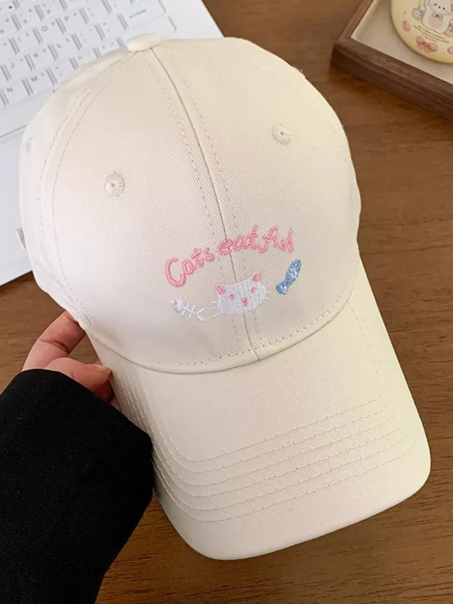 Cream baseball cap with embroidered cat and fish design and text.