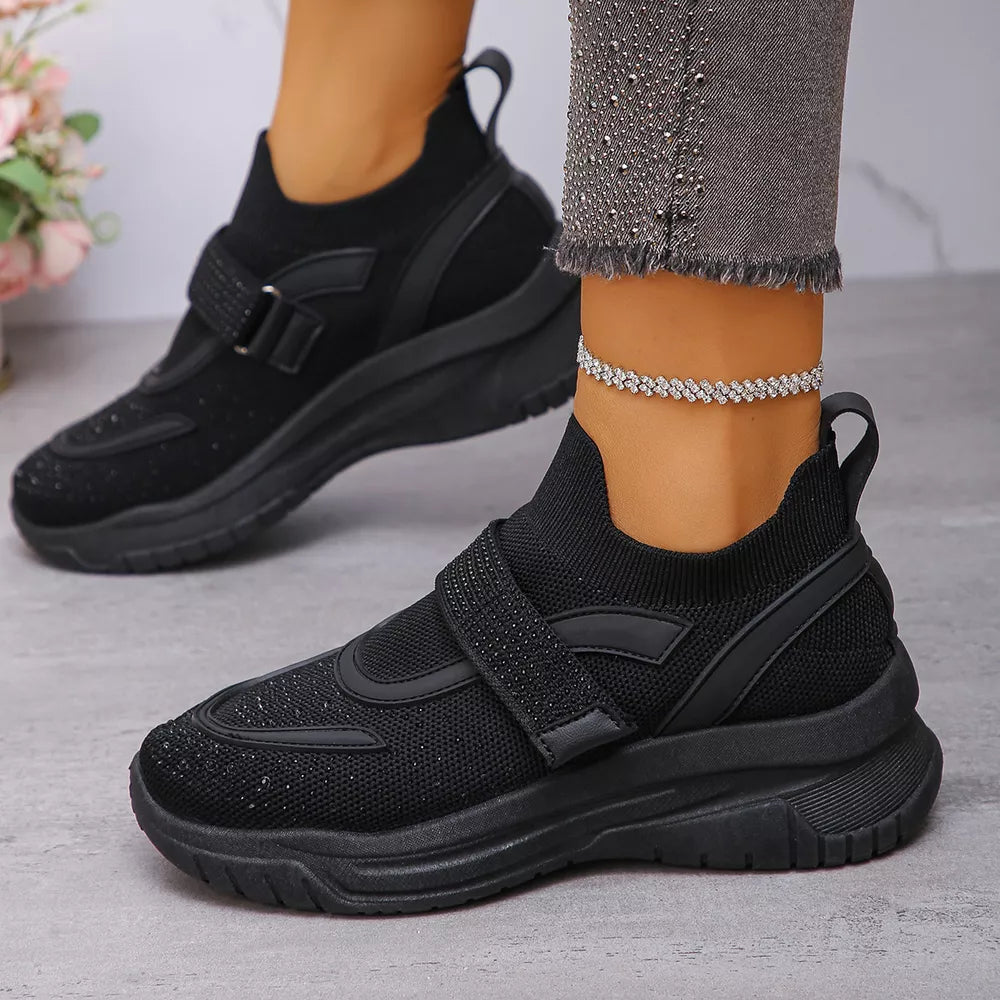 Black mesh slip-on sneakers with adjustable strap and subtle sparkle detail.