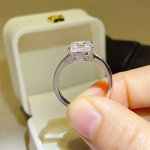 Silver ring with emerald cut diamond and baguette accents on a white ring box.