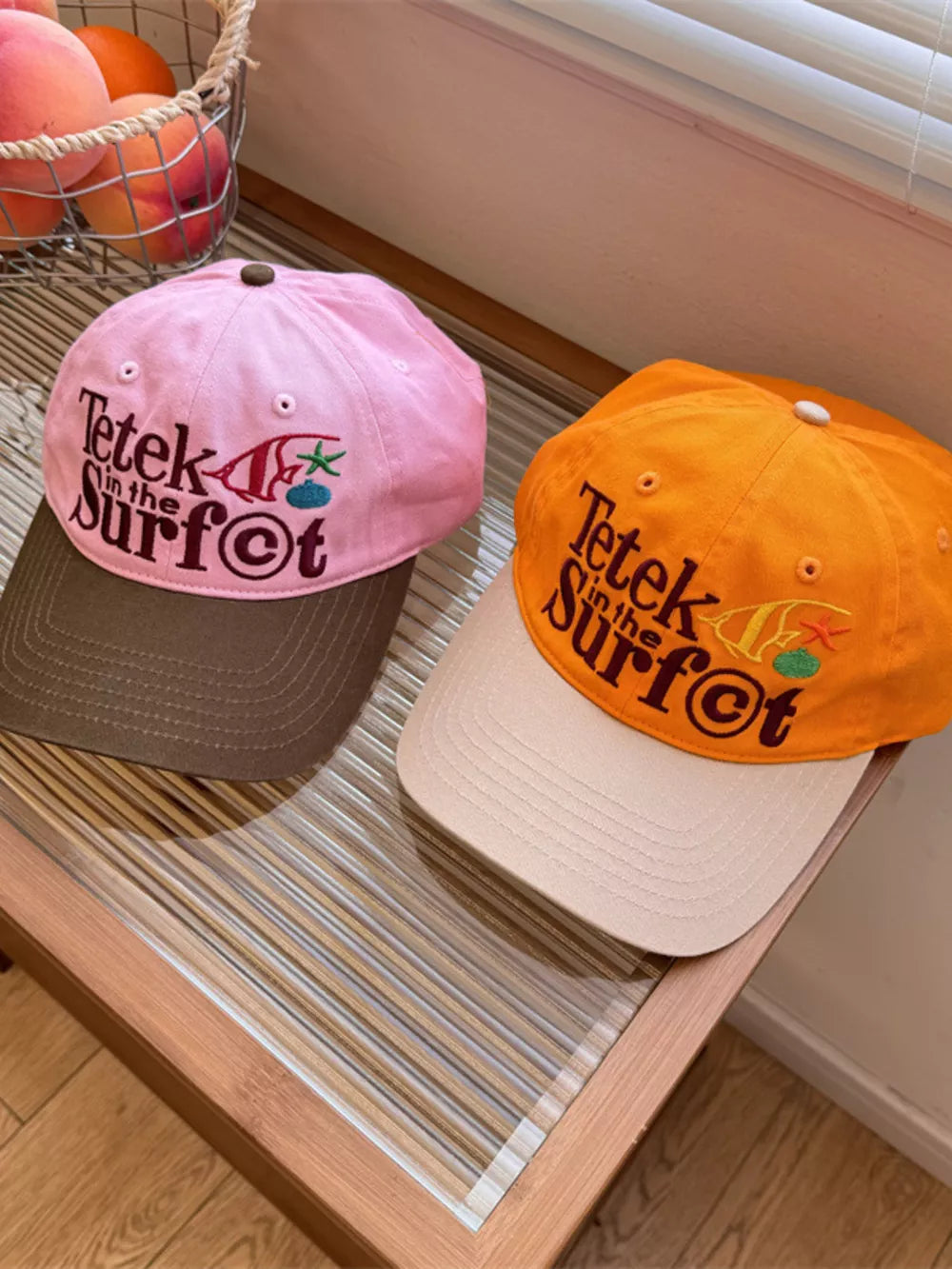 Pink and orange cotton baseball caps with embroidered "Tetek in the Surf" graphic.