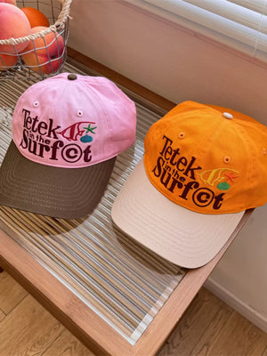 Pink and orange cotton baseball caps with embroidered "Tetek in the Surf" graphic.